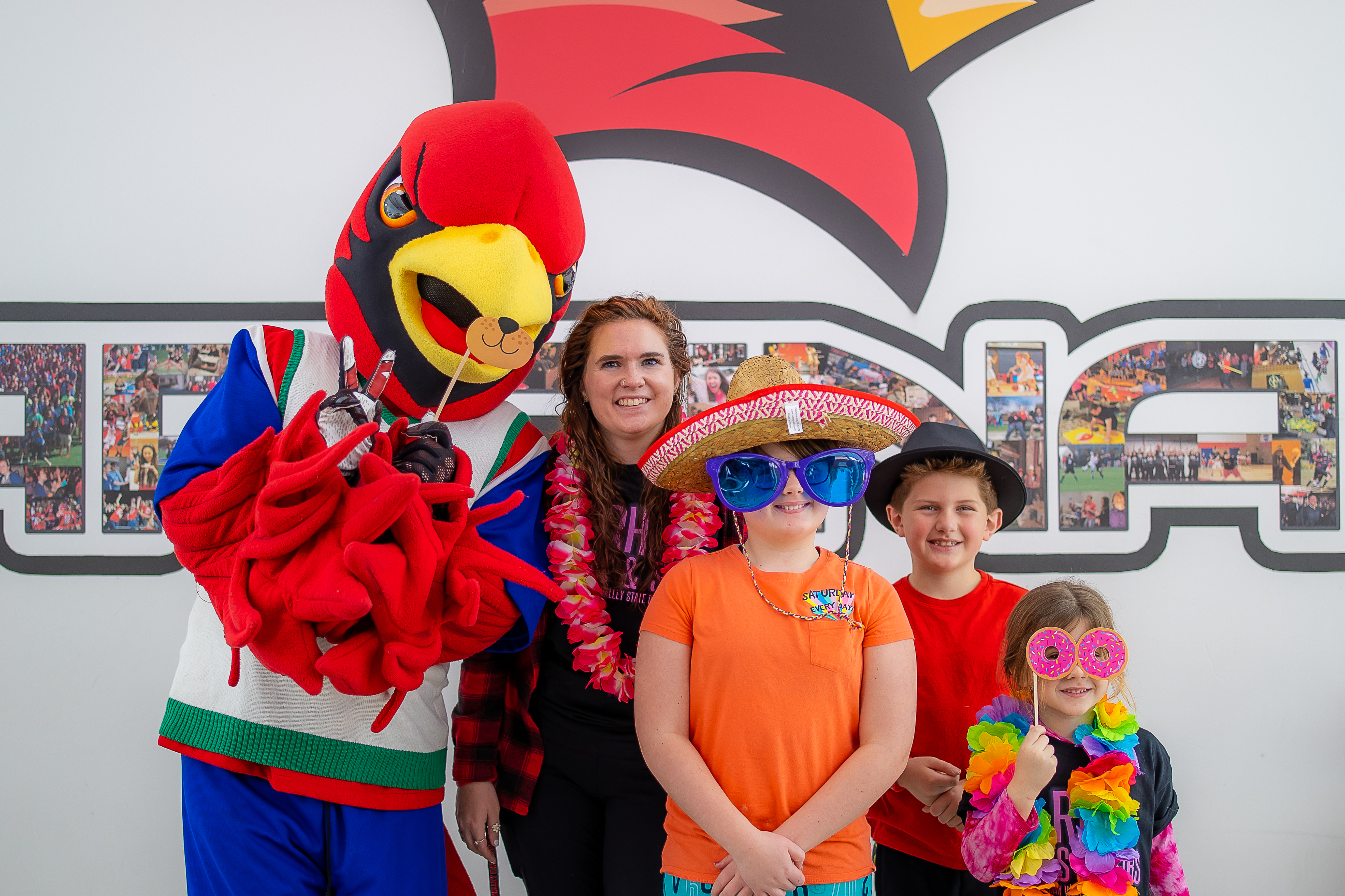 Young family members of an SVSU student posing with Coop the Cardinal in front of an SVSU backdrop.